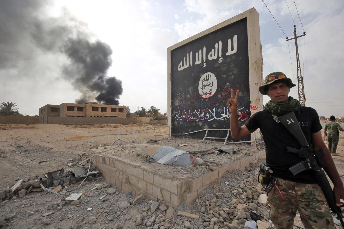 Iraqi fighters stand next to a wall bearing the Daesh flag as they enter the city of Al-Qaim, in Iraq’s western Anbar province near the Syrian border as they fight against remnant pockets of Daesh militants. (AFP)