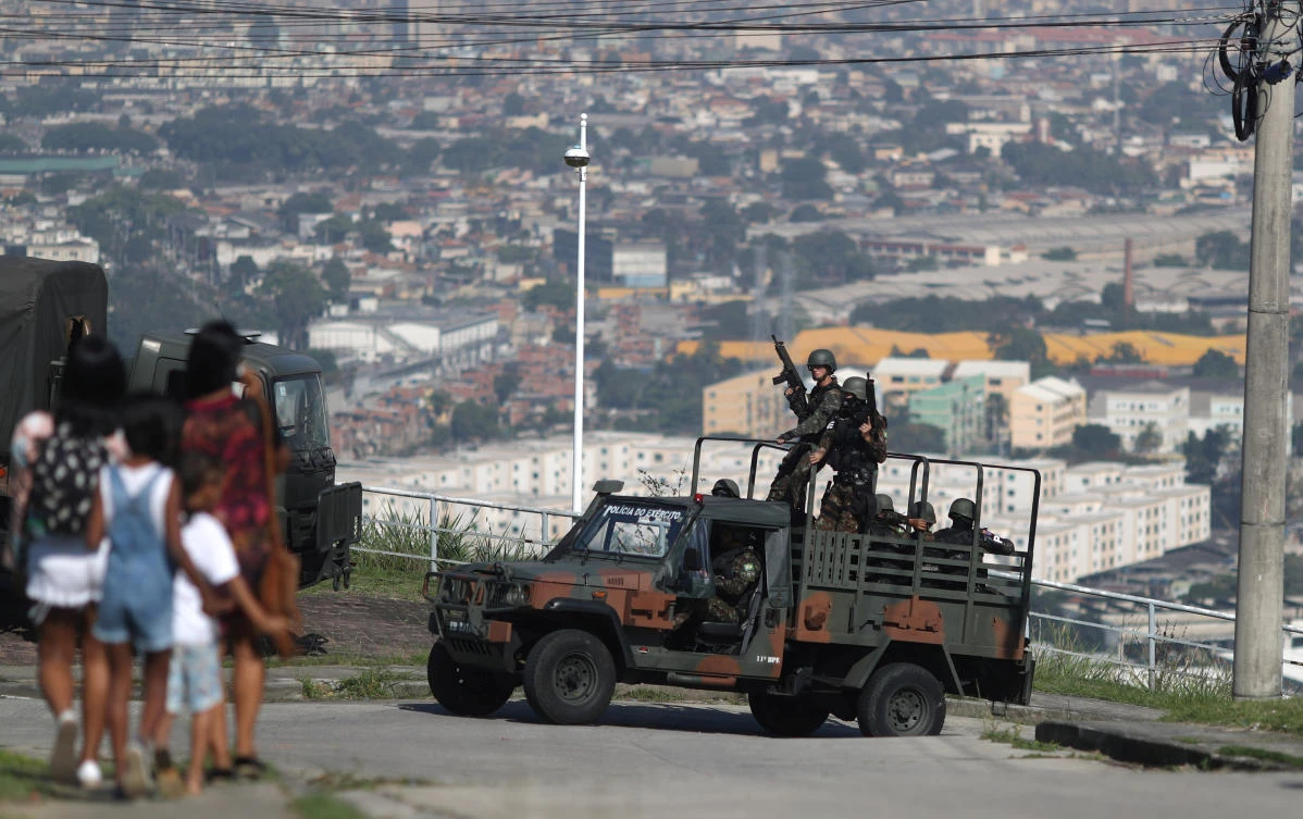 Residents walk past soldiers during an operation against drug dealers in the Alemao district of Rio de Janeiro, in Brazil. (Reuters)