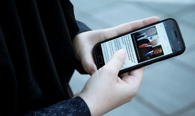 A woman displays photos of US President Donald Trump as she follows the news on her mobile phone in Tehran, Iran, in this October 13, 2017 file photo. (Reuters)