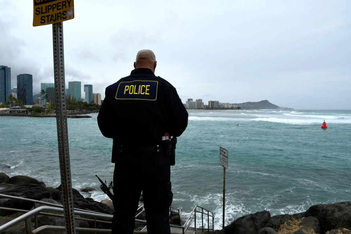 A police officer monitors the water conditions and warns surfers about the conditions as Hurricane Lane approaches Honolulu on Thursday, August 23. (Reuters)
