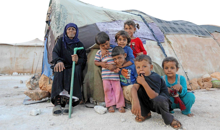 An elderly woman and children sit in front of a tent in a camp for the displaced from Idlib's southern province and Hama's northern provice, in Kafr Dariyan situated at a short distance from Syria's border with Turkey, on August 26, 2018. (AFP / OMAR HAJ KADOUR)