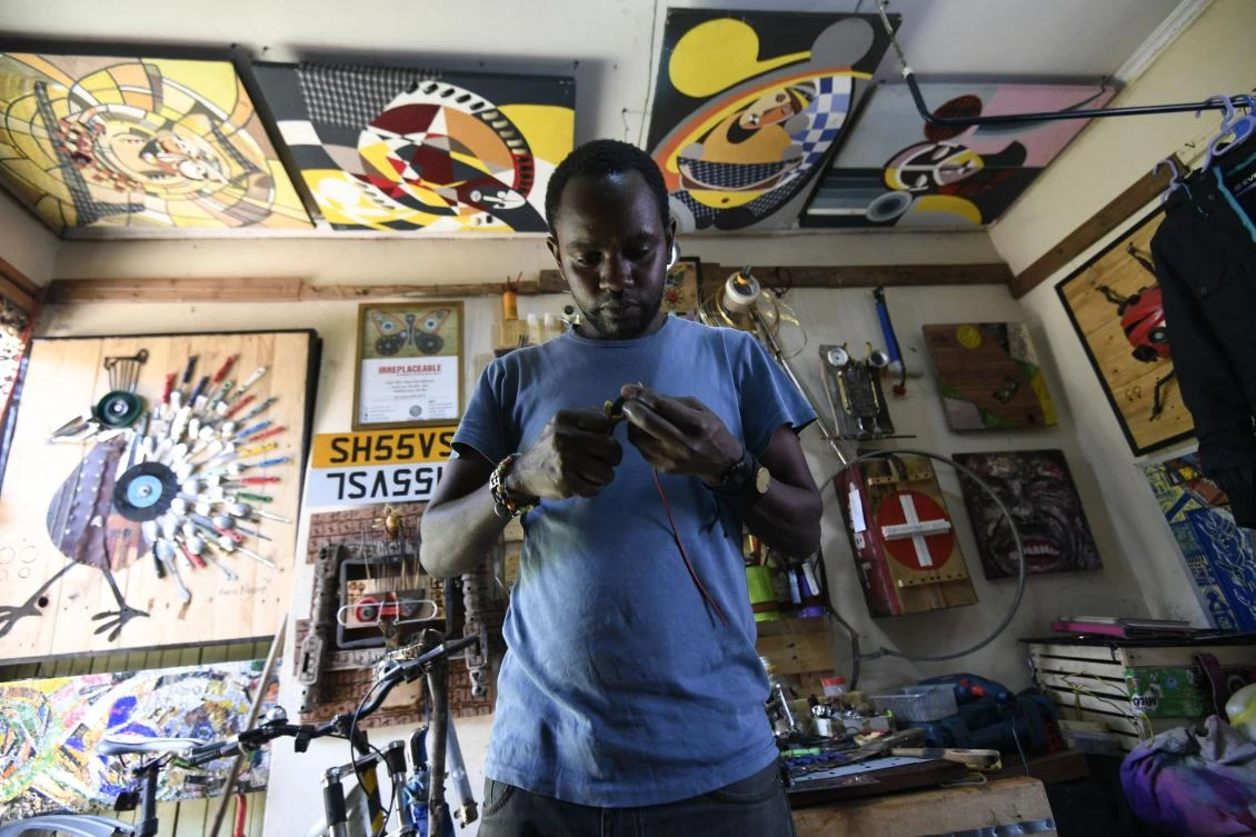 In a room that is both home and studio, Evans Ngure works on a sculpture, a fantastical fish fabricated from found objects: wooden spoons, broken scissors and an old machete. (AFP)