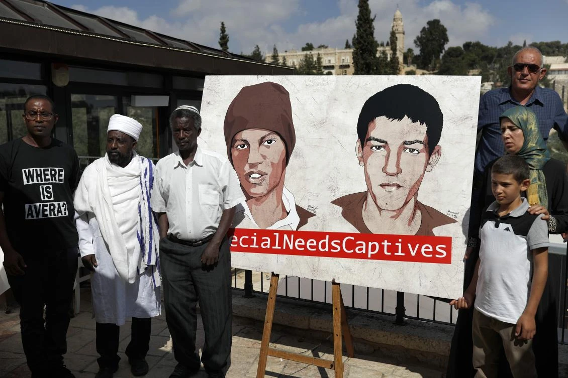 Relatives of Hisham Al-Sayed (C-R) and Avera Mengistu (C-L), two Israelis held by Hamas in Gaza since 2014, pose for a picture next to a painted poster depicting them after a press conference organised by the captives' families calling for their release, in Jerusalem on September 6, 2018. (AFP)