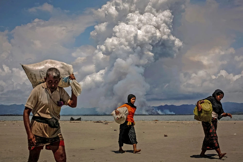 Smoke is seen on the Myanmar border as Rohingya refugees walk on the shore after crossing the Bangladesh-Myanmar border by boat through the Bay of Bengal, in Shah Porir Dwip, Bangladesh September 11, 2017. (Reuters)