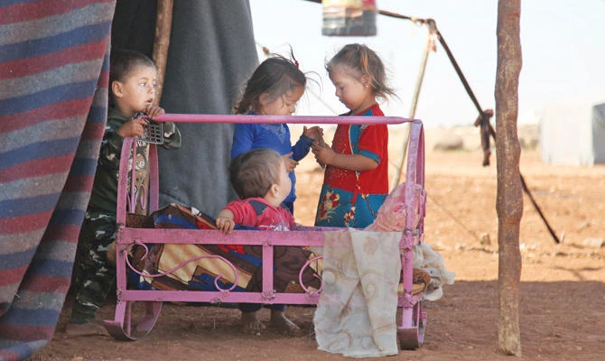 Children play next to a metal crib outside a tent at a camp for displaced civilians in the Idlib province. (AFP)