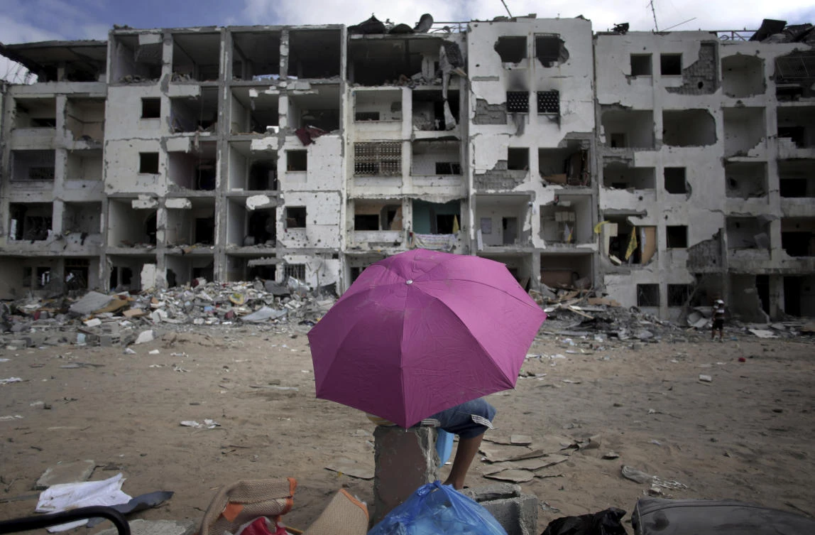 In this Aug. 11, 2014 file photo, a Palestinian boy holds an umbrella as he rests in front of the damaged Nada Towers residential neighborhood in the town of Beit Lahiya, northern Gaza Strip. (File/AP/Khalil Hamra)