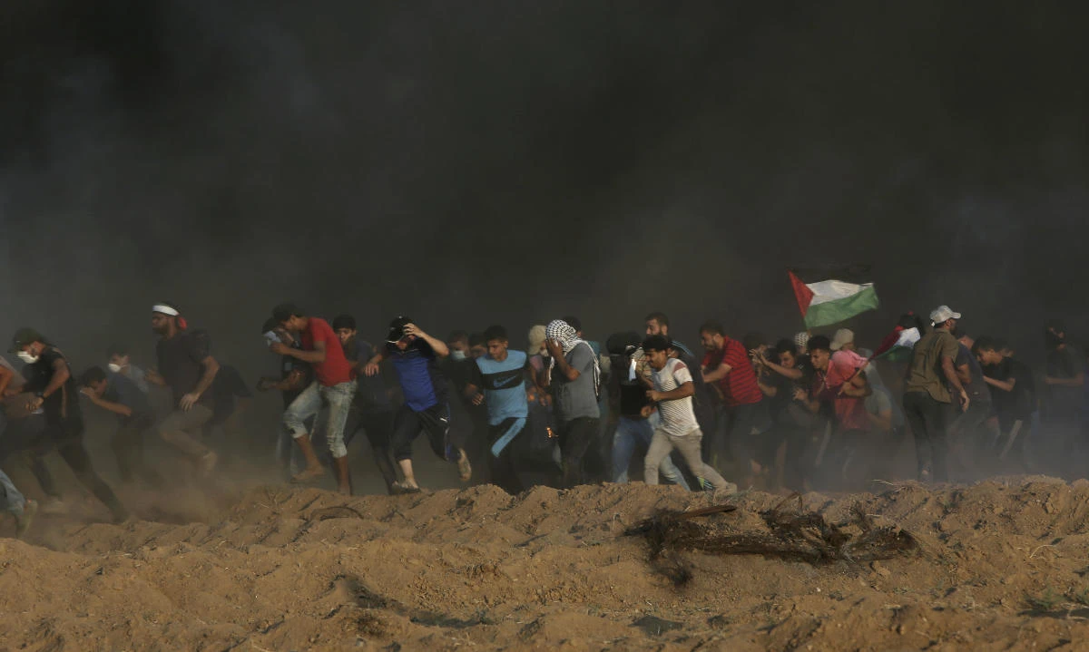 Protesters run to cover from teargas fired by Israeli troops while others burn tires near fence of Gaza Strip border with Israel during a protest east of Gaza City, Friday, Sept. 21, 2018. (AP)
