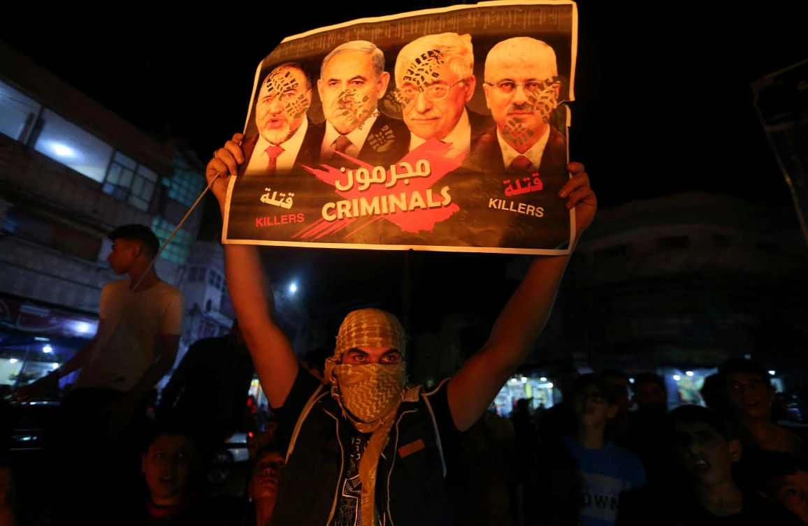 A demonstrator holds up a poster reading "criminals" and showing Palestinian Prime Minister Rami Hamdallah, Palestinian President Mahmoud Abbas, Israeli Prime Minister Benjamin Netanyahu and Israeli Defence Minister Avigdor Lieberman during a protest following Abbas's speech at the United Nations General Assembly, in Rafah in the southern Gaza Strip September 27, 2018. (Reuters)