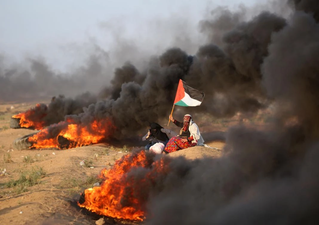 A Palestinian woman waves a national flag near burning tyres during clashes along the Israeli border fence, east of Gaza City on September 28, 2018. (AFP)