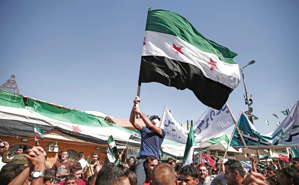 A Syrian man waves an opposition flag during an anti-regime protest, calling for the release of prisoners in the opposition-held town of Atareb, Aleppo. (AFP)