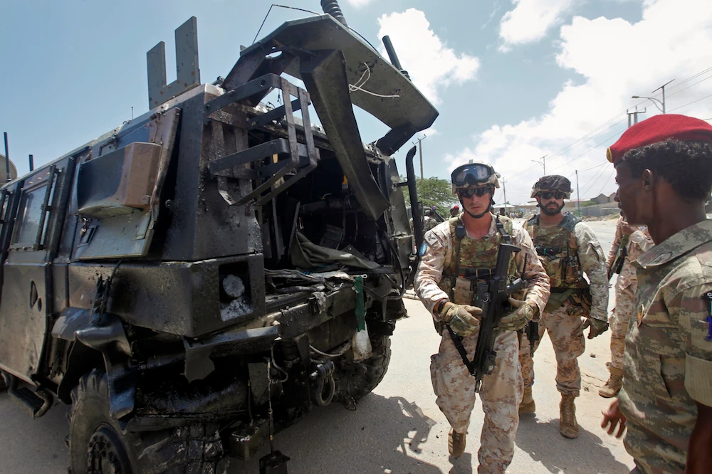 Two members of the Italian military and a Somali soldier, right, walk next to a damaged armored personnel carrier after an attack on a European Union military convoy in the capital Mogadishu, Somalia Monday, Oct. 1, 2018. (AP)