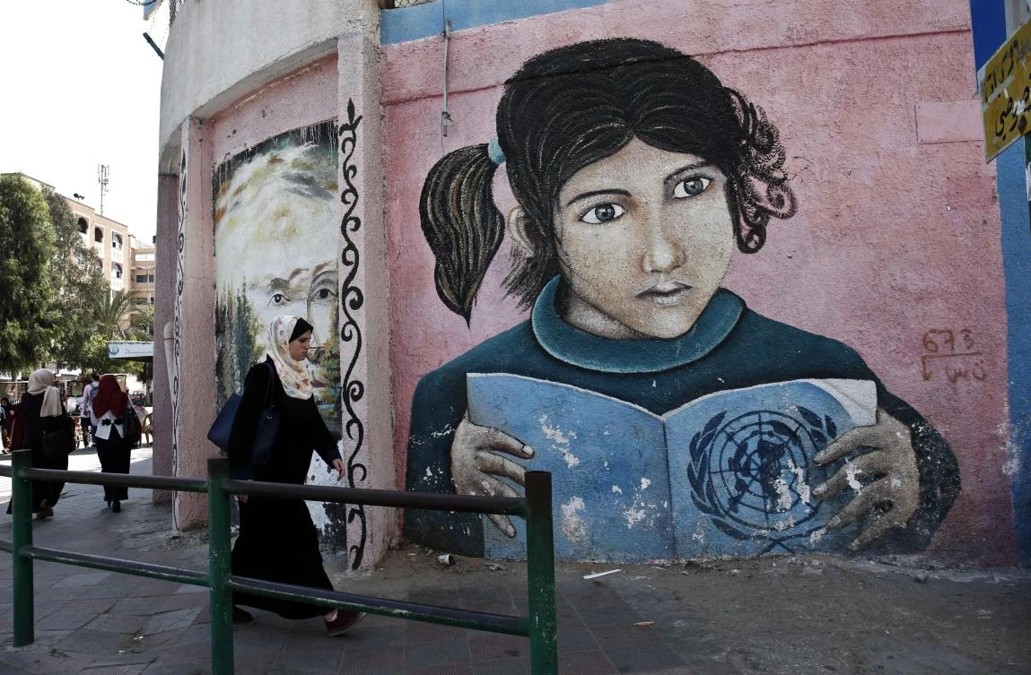 TOPSHOT - A Palestinian woman walks in front a mural painted on a wall of the headquarters of the United Nations Relief and Works Agency (UNRWA) in Gaza City on October 2, 2018, closed in protest against job cuts announced by the UNRWA. Earlier this year, the United States, by far the biggest contributor to the agency, announced it was halting its funding to the organisation, which it labelled "irredeemably flawed". / AFP / SAID KHATIB