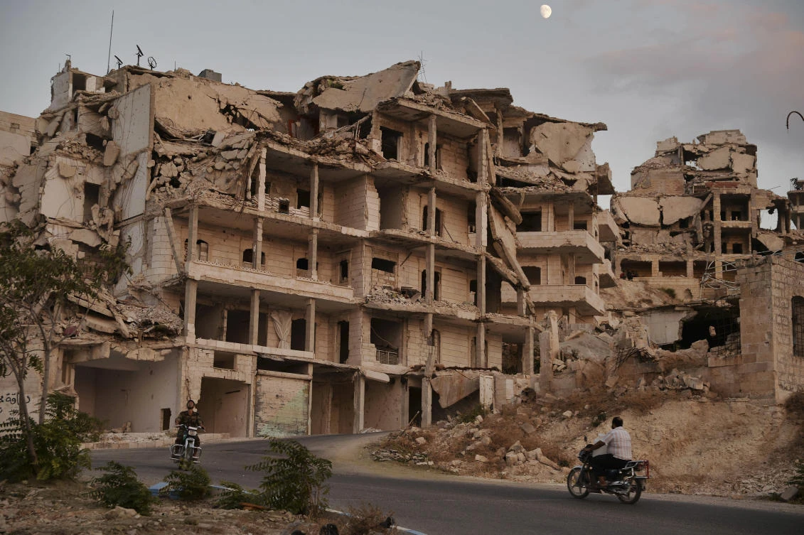 Motor cycles ride past buildings destroyed during the fighting in a northern town in Idlib province, Syria. (File photo / AP)