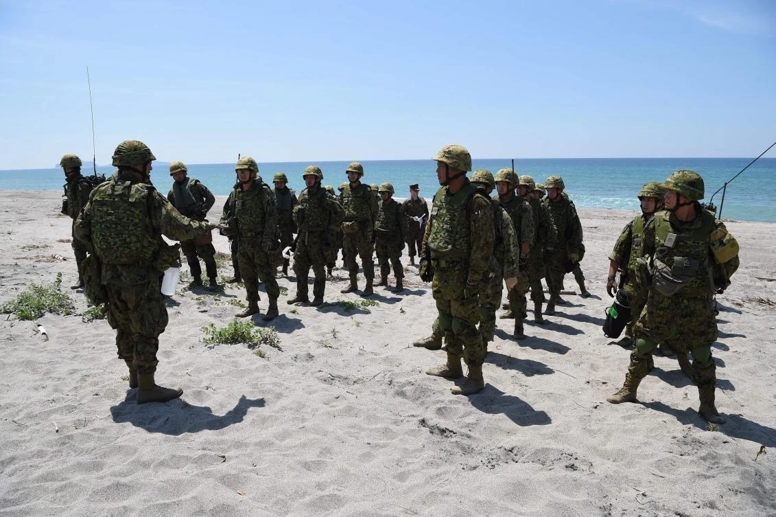 Fifty unarmed Japanese soldiers in camouflage marched behind their four armored vehicles and picked up Filipino and American troops playing the role of wounded combatants. (AFP / Ted Albije)