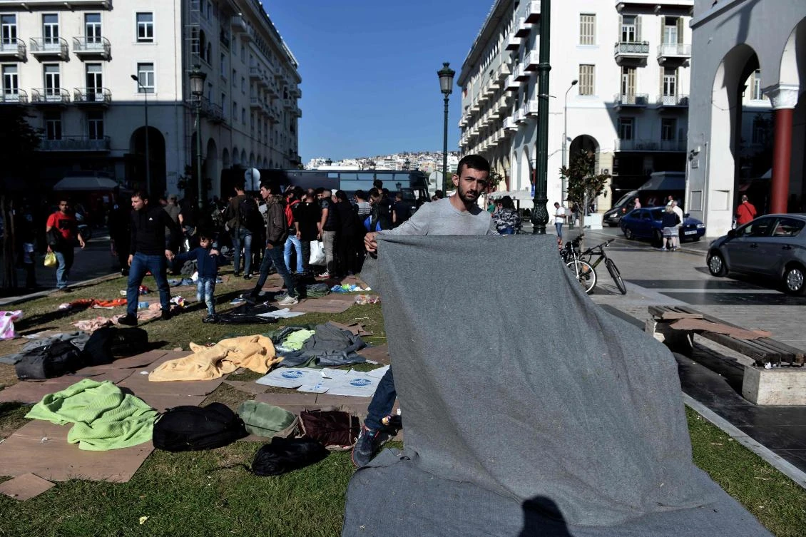 A migrant picks up his blanket outside of the police station in Thessaloniki's Aristotelous main square on October 8, 2018. (AFP)