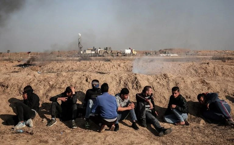 Palestinian demonstrators sit along the border with Israel as Israeli heavy machinery, background, work to search for tunnels in the southern Gaza strip city of Khan Yunis in February 2018. (AFP)