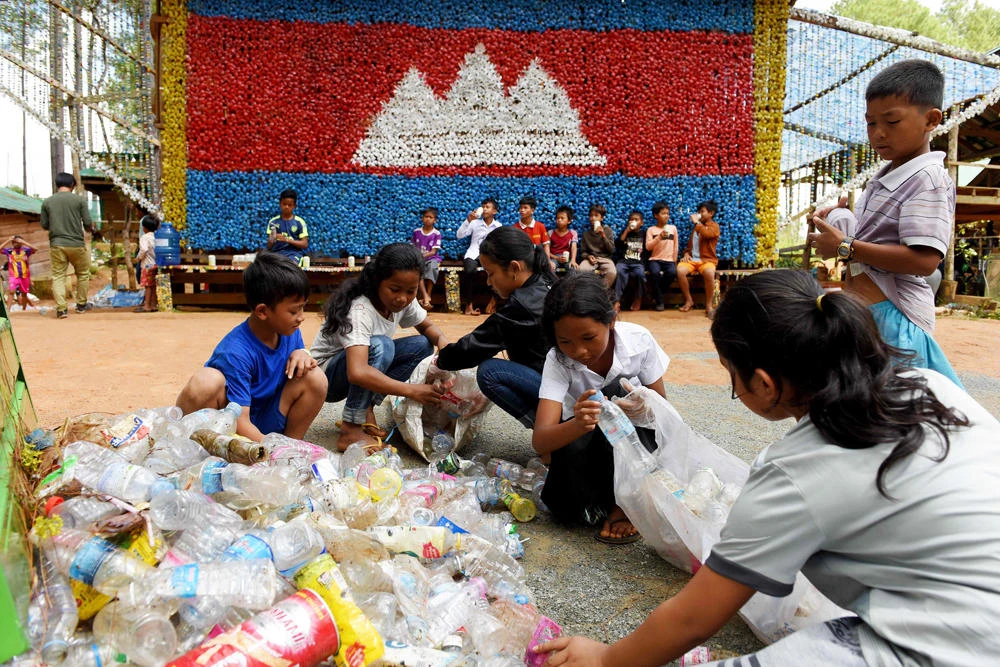 This photo taken on October 1, 2018 shows students sorting out salvaged plastic water bottles in front of a Cambodian flag made from recycled plastic materials at the Coconut School at Kirirom national park in Kampong Speu province. (AFP / TANG CHHIN SOTHY)