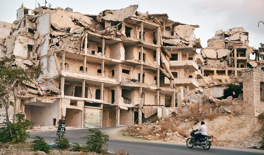In this file photo, Motorcycles ride past buildings destroyed during the fighting in the northern town of Ariha, in Syria’s Idlib province. (AP)