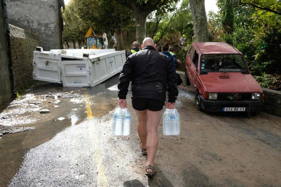 Residents carrying packs of bottled water walk past damaged cars on October 15, 2018 in Villegailhenc, near Carcassone, southern France, following heavy rains that saw rivers bursting banks. (AFP)