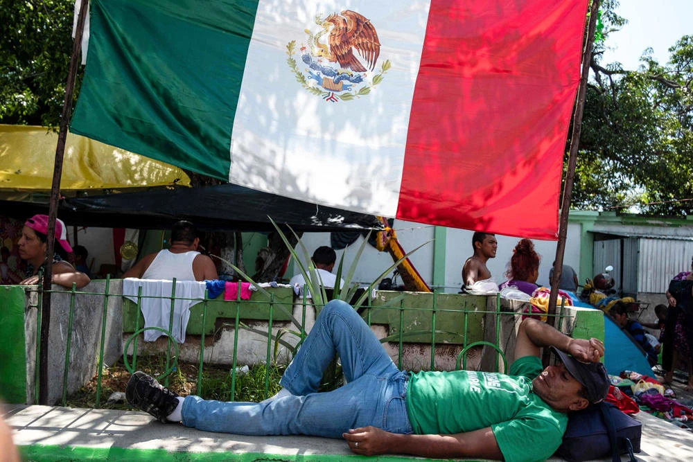 Honduran migrants taking part in a caravan heading to the US, rest next to a Mexican national flag during a stop in Pijijiapan, Chiapas state, Mexico, on October 25, 2018. (AFP / Guillermo Arias)