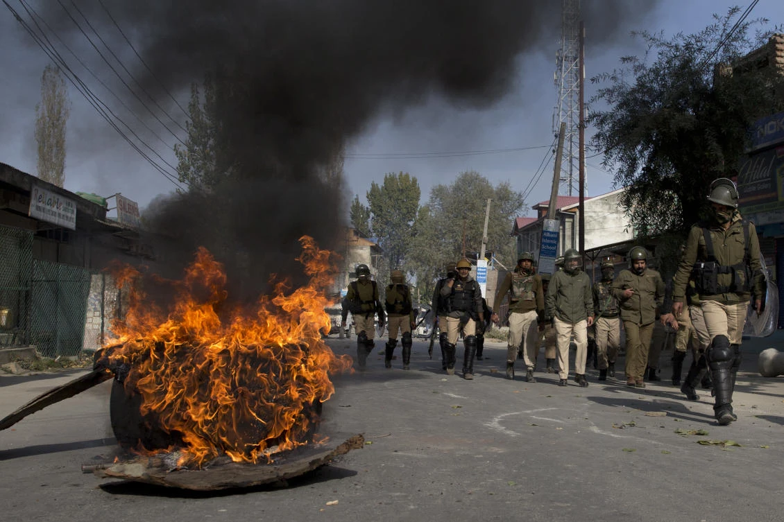 Indian police men walk past burning tar coal filled drum set as road blockade by Kashmiri protesters near the site of gunbattle in Srinagar on Wednesday, October 24. (AP)