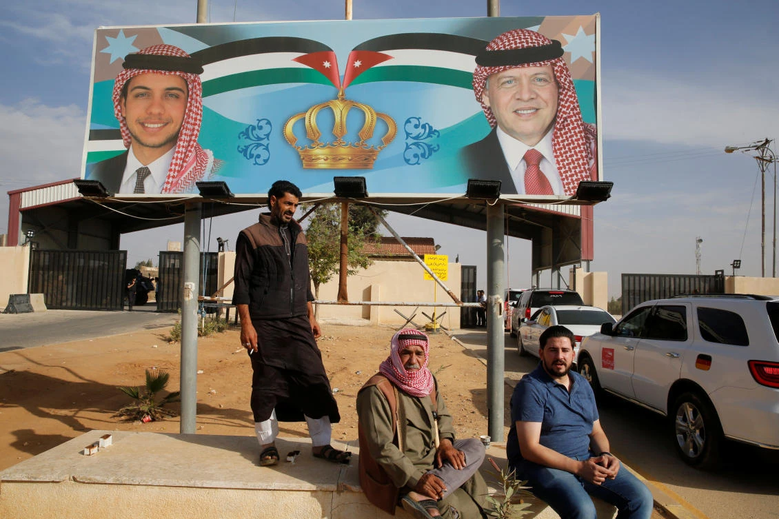 People sit next of a billboard with a picture of Jordan's King Abdullah and Crown Prince Hussein as they wait to travel to Syria at Jordan's Jaber border crossing, near Syria's Nassib checkpoint, near Mafraq, Jordan, October 25, 2018. (Reuters)