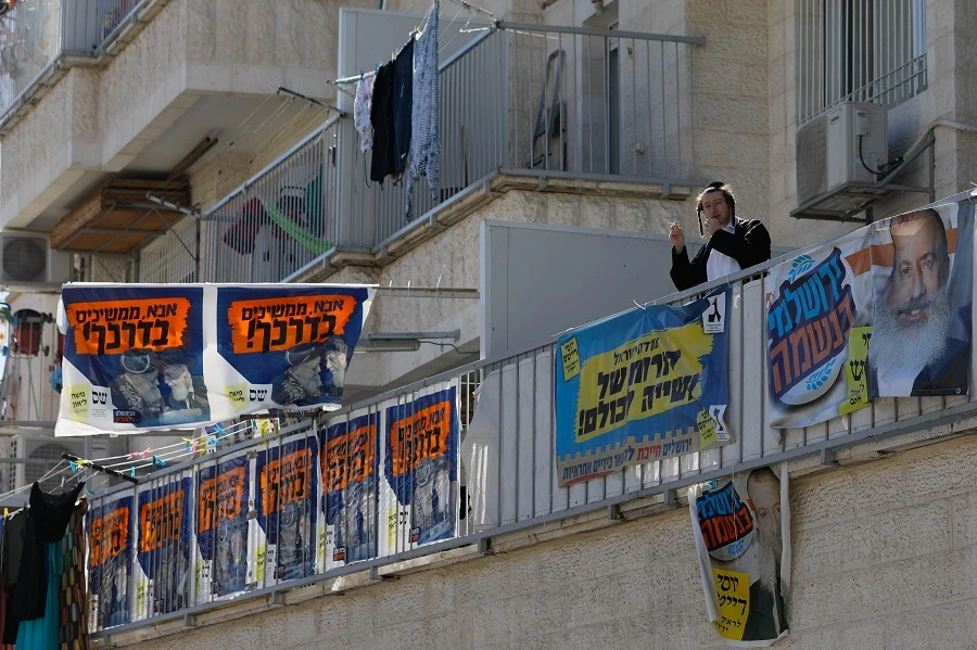 An Ultra-Orthodox Jewish man smokes a cigarette on a balcony in a building bearing election campaign posters for the upcoming Jerusalem municipal elections, in Jerusalem on October 28, 2018. (AFP)