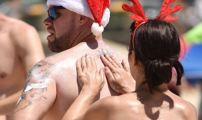 This photo taken on December 25, 2016 shows a couple applying suntan lotion whilst wearing Christmas hats on Bondi Beach to mark Christmas Day in Sydney. (AFP)