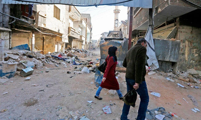 People walk amid rubble of destroyed buildings near a cover to protect civilians from sniper bullets in a street in Tadamun neighbourhood near the Palestinian Yarmuk camp in the south of the Syrian capital of Damascus on November 3, 2018. (AFP)