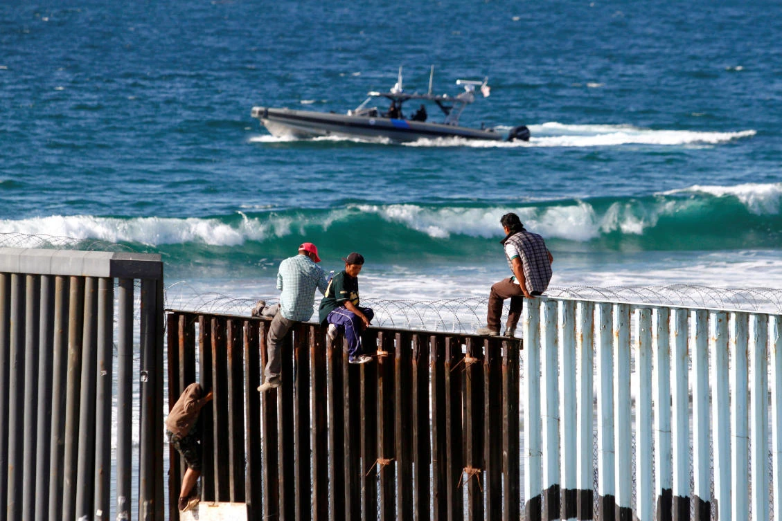 Migrants, part of a caravan of thousands trying to reach the U.S., sit on top of the border fence between Mexico and the United States, in Tijuana. (Reuters)