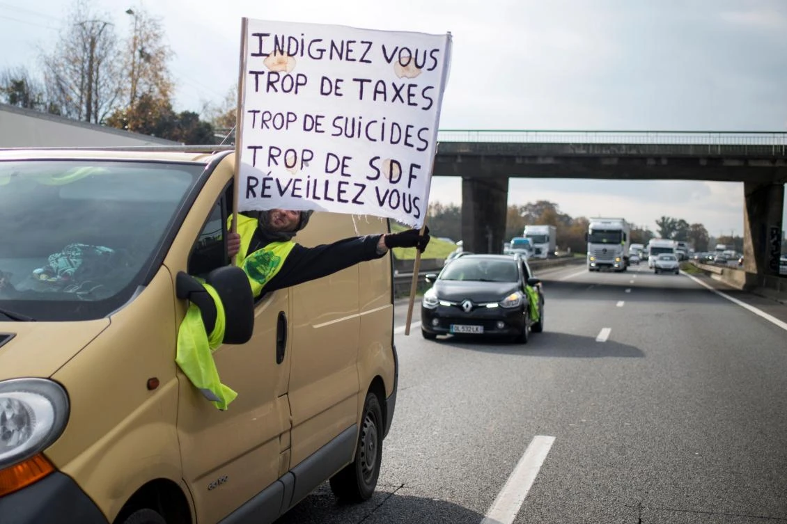 A protester brandishes a banner reading “Rebel, too many taxes, too many suicides, too many homeless, wake-up” during a traffic slow down operation on a fourth day of action by the “yellow vest” (Gilets Jaunes in French) movement against high fuel prices which has mushroomed into a widespread protest against stagnant spending power under French President, in Rennes western France. (AFP)
