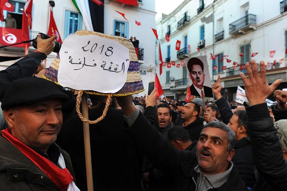 Tunisian workers hold up a basket with text reading in Arabic: "the basket is empty" while shouting slogans against the government in front of the Tunisian General Labour Union (UGTT) headquarters in Tunis as they mark the seventh anniversary since the uprising that launched the Arab Spring, on January 14, 2018. (File/AFP)