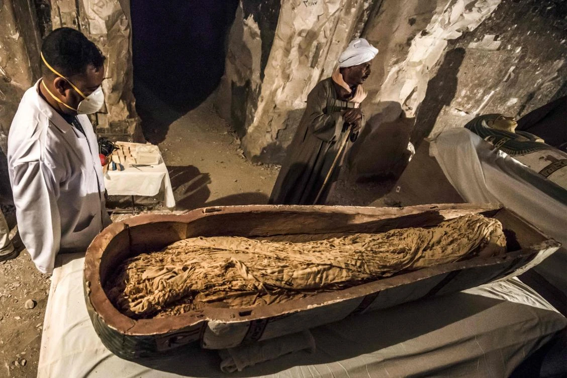 Egyptian workers and archaeologists standing next to an opened intact sarcophagus containing a well-preserved mummy of a woman named “Thuya” wrapped in linen, discovered by a French mission at the site of Tomb TT33 which dates to the 18th dynasty (16th-13th century BC) at Al-Assasif necropolis on the west bank of the Nile north of the southern Egyptian city of Luxor. (AFP)