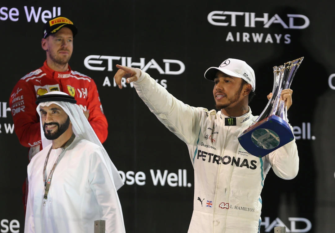 Lewis Hamilton celebrates with a trophy after winning the Abu Dhabi Grand Prix as second place Ferrari's Sebastian Vettel looks on. (Reuters)