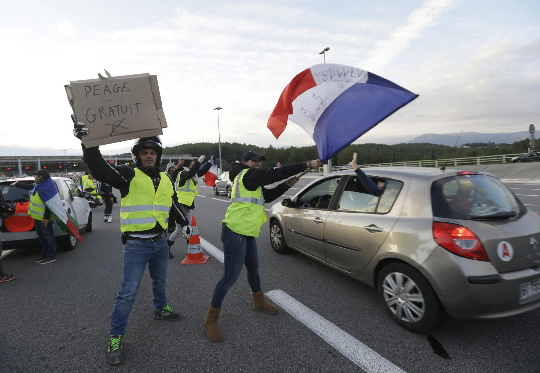 In this Nov. 19, 2018 file photo, protesters known as the yellow jackets, wave a French flag and a poster reading "Free toll" as they open the toll gates on a motorway in Antibes, southern France. (AP)