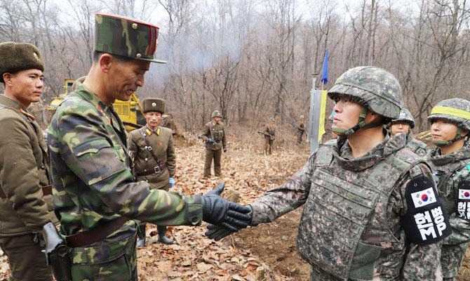 This handout taken on an unconfirmed date and released by the South Korean Defence Ministry on November 22, 2018 shows a South Korean soldier (R) shaking hands with a North Korean soldier (L) near the Military Demarcation Line (yellow signboard) during a recent operation to construct a tactical road to support a joint war remains recovery project in the Demilitarized Zone (DMZ) dividing the two Koreas in Cheorwon. (AFP)