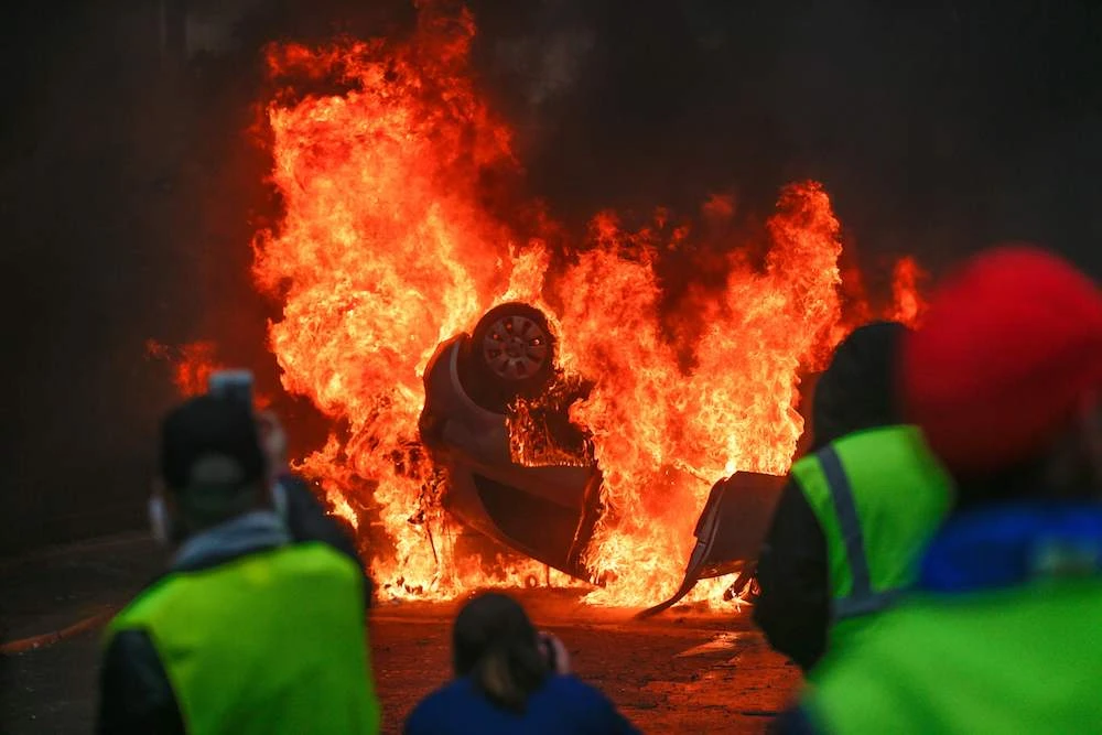 Demonstrators stand in front of a burning car during a protest of Yellow vests (Gilets jaunes) against rising oil prices and living costs, on December 1, 2018 in Paris. (AFP)
