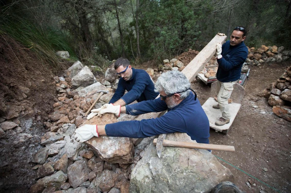 Some men build a wall using the dry stone technique in Esporles on the Spanish Balearic Island of Mallorca on December 11, 2018. The art of dry stone walling, inscribed in 2018 on the Representative List of the Intangible Cultural Heritage of Humanity, (sometimes called drystack) is a building method by which structures are constructed from stones without any mortar to bind them together. Dry stone structures are stable because of their unique construction method, which is characterized by the presence of a load-bearing facade of carefully selected interlocking stones. / AFP / JAIME REINA