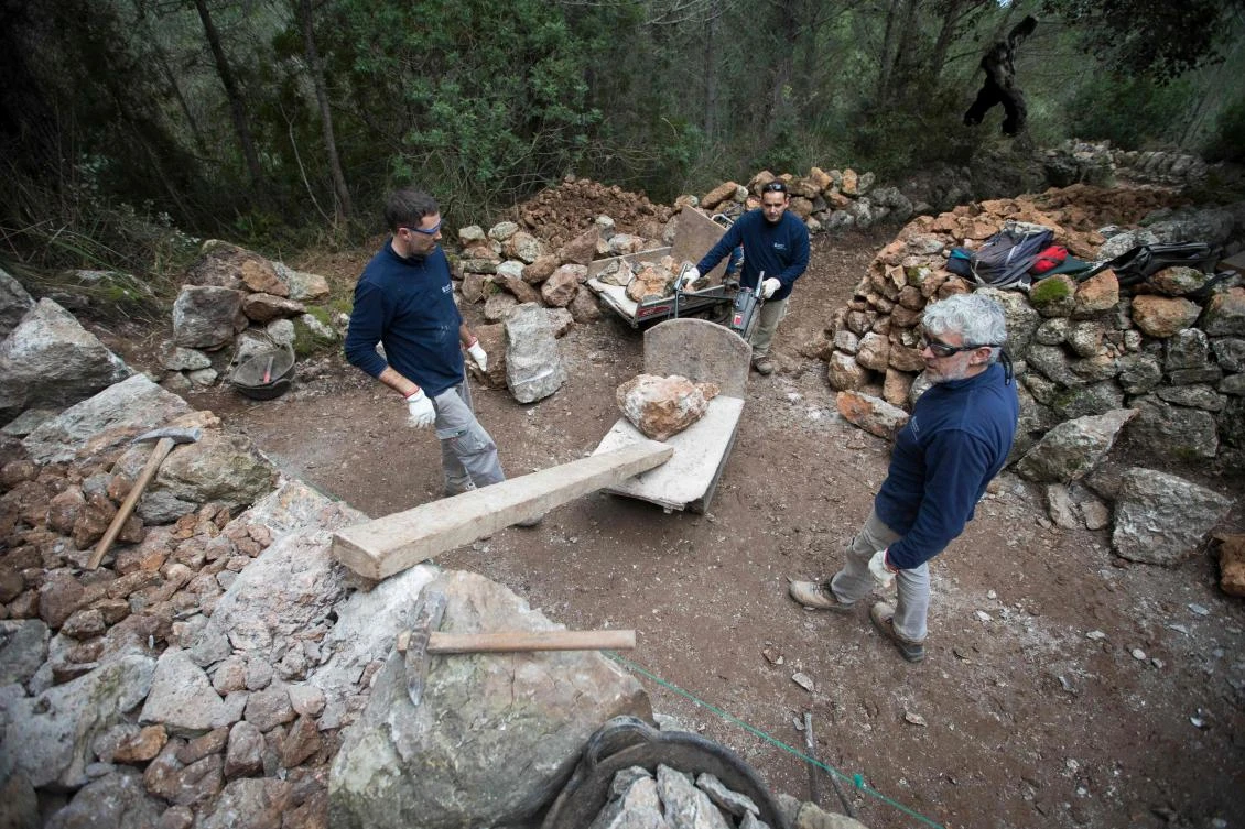 Some men build a wall using the dry stone technique in Esporles on the Spanish Balearic Island of Mallorca on December 11, 2018. The art of dry stone walling, inscribed in 2018 on the Representative List of the Intangible Cultural Heritage of Humanity, (sometimes called drystack) is a building method by which structures are constructed from stones without any mortar to bind them together. Dry stone structures are stable because of their unique construction method, which is characterized by the presence of a load-bearing facade of carefully selected interlocking stones. / AFP / JAIME REINA