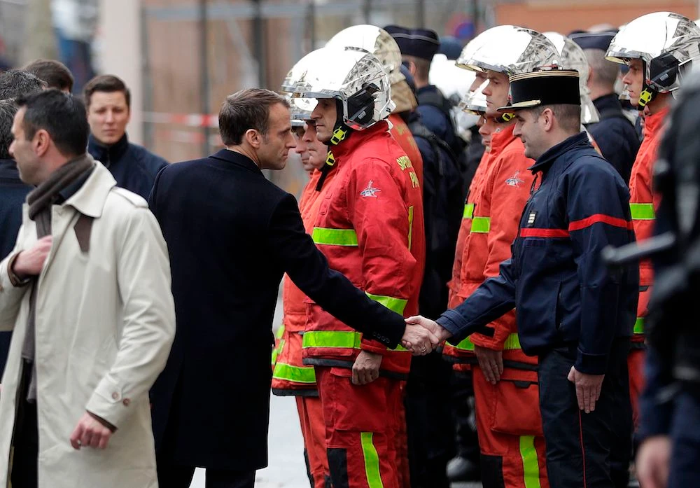 French President Emmanuel Macron (L) shakes hands with a firefighter during a visit in the streets of Paris on December 2, 2018, a day after clashes during a protest of Yellow vests (Gilets jaunes) against rising oil prices and living costs. (AFP)