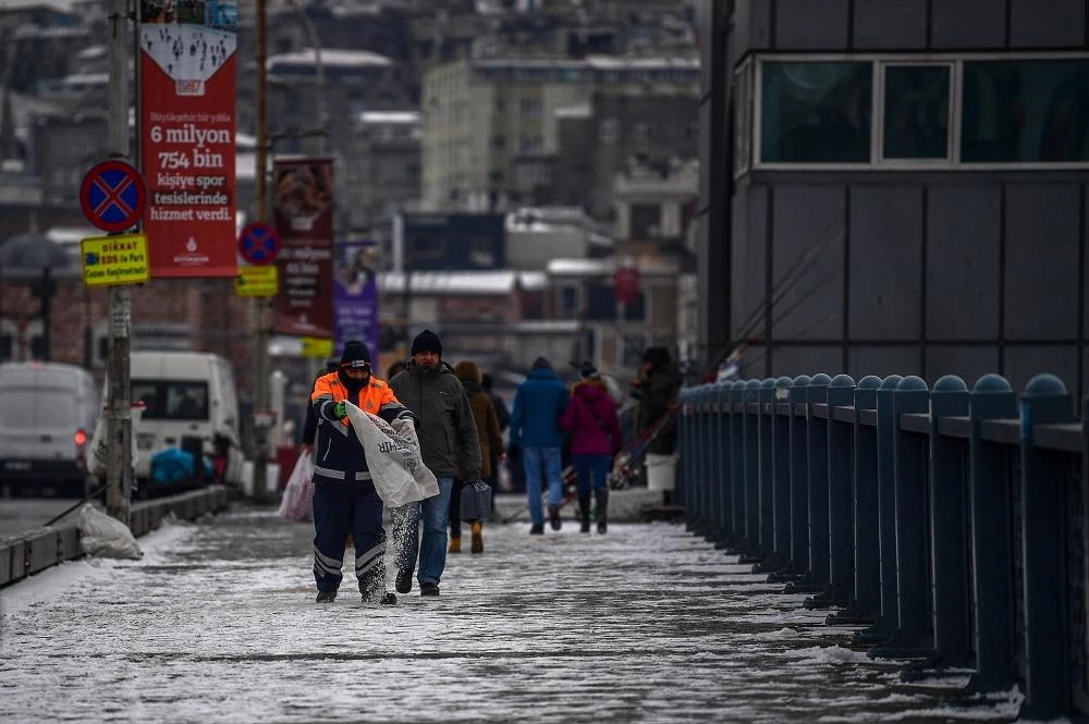 A municipality worker throws salt on snow as people walk on the Galata bridge on March 1, 2018 during snowy day in Istanbul. (File/AFP)