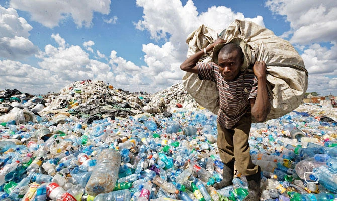 In this photo taken Wednesday, Dec. 5, 2018, a man walks on a mountain of plastic bottles as he carries a sack of them to be sold for recycling after weighing them at the dump in the Dandora slum of Nairobi, Kenya. (AP)