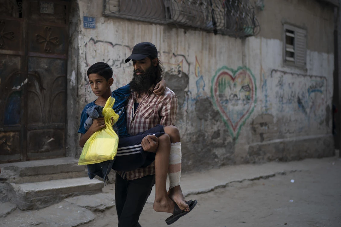 In this Sept. 16, 2018, photo, Raed Abu Khader, right, carries his 12-year-old son Mohammed as they return from the hospital in Gaza City. Mohammed was shot in the leg at one of the demonstrations on Gaza strip’s border with Israel. (Felipe Dana/AP)
