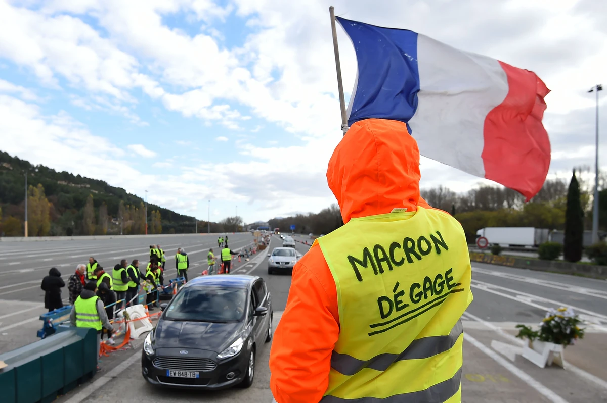 A man with a sign reading “Macron resign” waves a French flag as “yellow vests” (Gilets jaunes) protesters gather to protest against rising oil prices and living costs at the highway’s toll of La Barque, on December 9, 2018, near Marseille, southern France. (AFP)