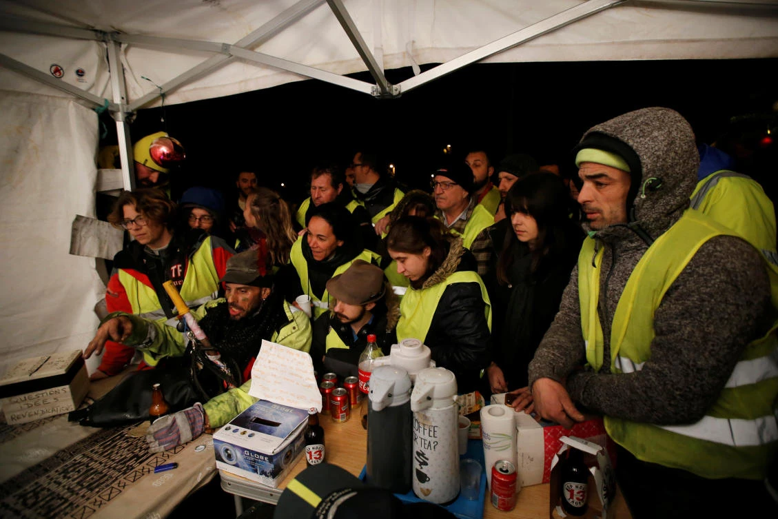 Protesters wearing yellow vests watch French President Emmanuel Macron on a TV screen at the motorway toll booth in La Ciotat, near Marseille. (Reuters)
