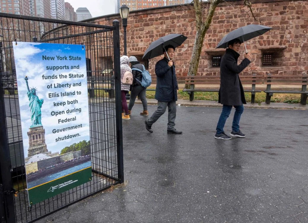 People walk past a sign announcing that New York funds are keeping the Statue of Liberty and Ellis Island open for visitors as the US government shutdown enters its third week. (AFP)