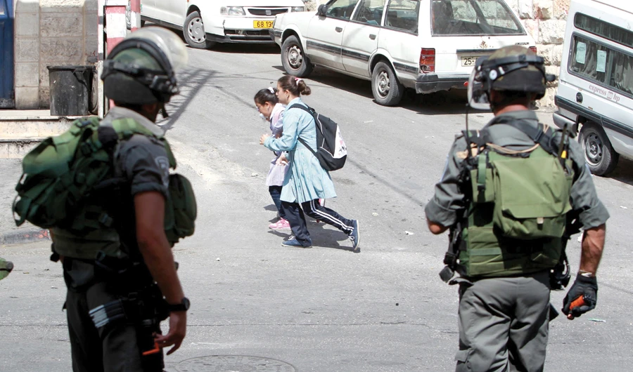 Israeli border police watch as Palestinian young girls walk on a street in Abu Dis, on the outskirts of east Jerusalem. (AFP)