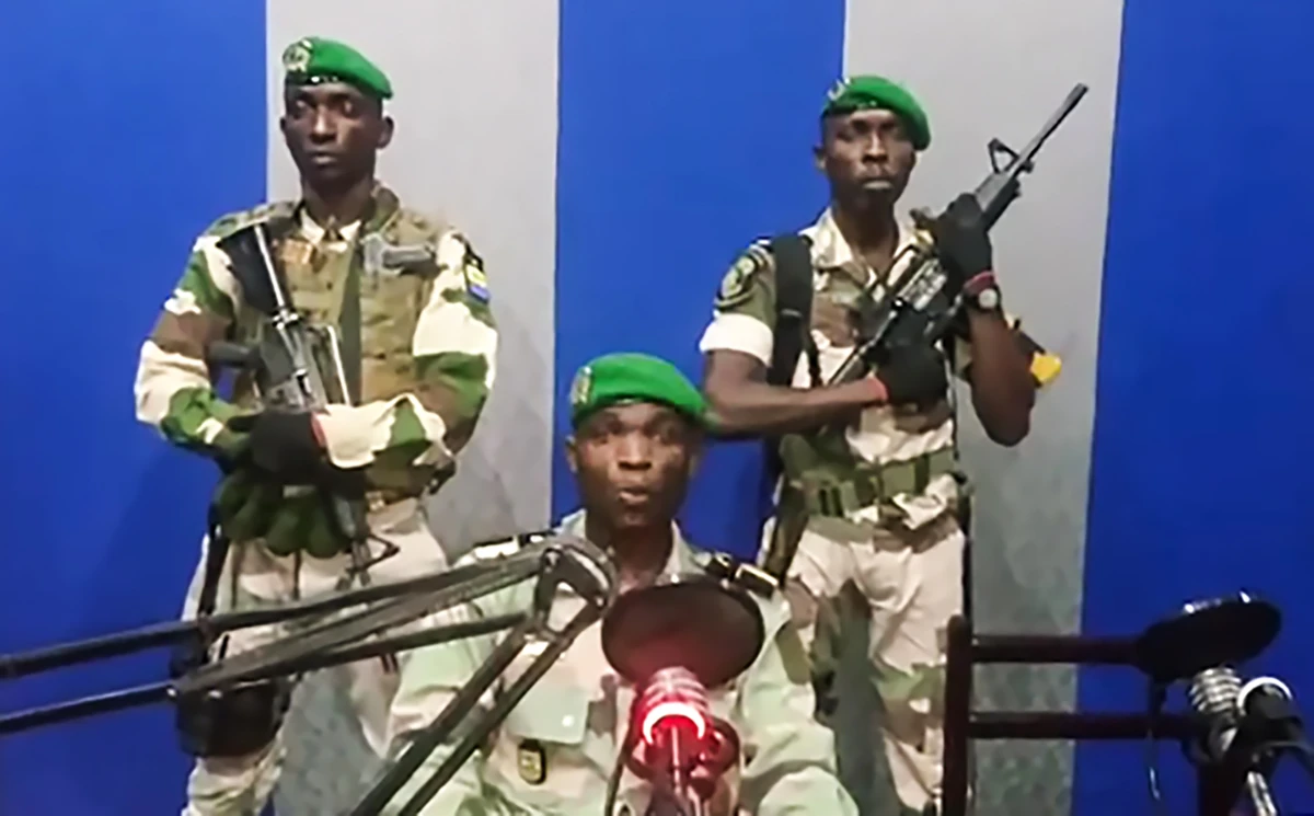 A soldier who identifies himself as Lieutenant Kelly Ondo Obiang, center, reads a message on state radio exhorting the Gabonese people to join them while two other soldiers stand on guard. (AFP)