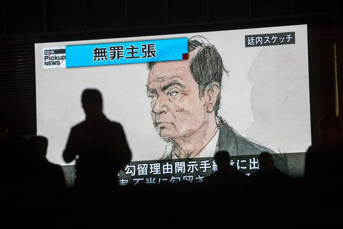 Pedestrians pass by a television screen showing a news program displaying a sketch of former Nissan chief Carlos Ghosn in the courtroom, in Tokyo on January 8, 2019, as the headline reads in Japanese “Innocence claim.” (AFP)