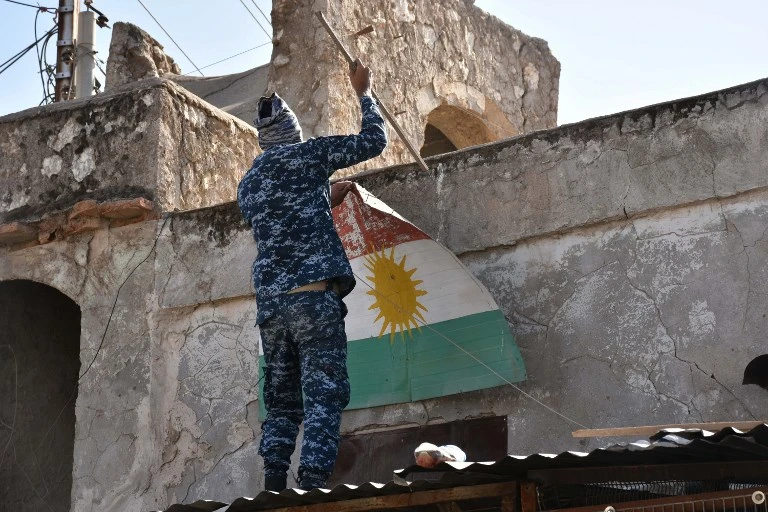 An Iraqi fighter loyal to the federal government attempts to remove a sheet metal sign painted with the colours of the Kurdish flag from a building in the region of Altun Kupri, about 50 kilometres (30 miles) from Arbil, capital of autonomous Iraqi Kurdistan, on October 20, 2017. (File/AFP)